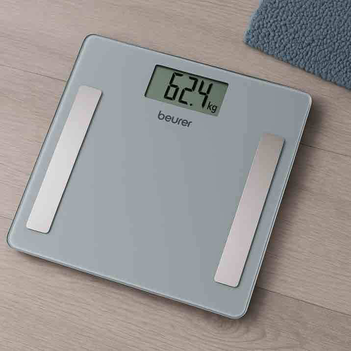 Moderni Beurer-henkilövaaka kylpyhuoneen lattialla, lasipintainen ja digitaalinen näyttö näkyvissä.