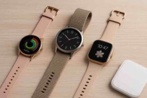 Kolme erilaista älykelloa on aseteltu vierekkäin vaalealle puupinnalle. Vasemmalla on pyöreänäyttöinen kultareunainen kello vaaleanpunaisella hihnalla ja värikkäällä aktiivisuusnäkymällä. Keskellä on perinteisen kellon näköinen malli tummalla analogisella kellotaululla ja hiekanvärisellä kudotulla hihnalla. Oikealla on neliömäinen kulta-reunainen älykello beigeillä hihnoilla ja näytöllä kukkakuviolla sekä kellonajalla 10:47.